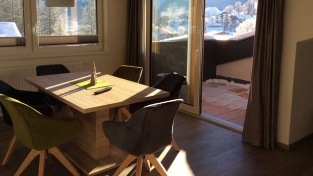Un coin repas avec une table et des chaises en bois, de grandes fenêtres et une vue sur un paysage enneigé.