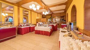 A buffet setup with multiple tables covered in red tablecloths, a counter with a red front, and a variety of food and drink containers. - Hotel Germania Gastein (Bad Hofgastein)