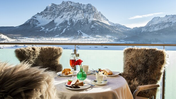 Une table garnie de plats et de boissons, une vue sur la montagne et des fauteuils recouverts de fourrure.