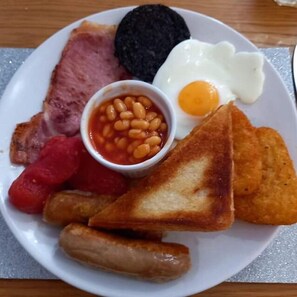 A plate with a variety of breakfast items including eggs, bacon, beans, toast, sausages, and a black pudding. - Rossall House (Blackpool)
