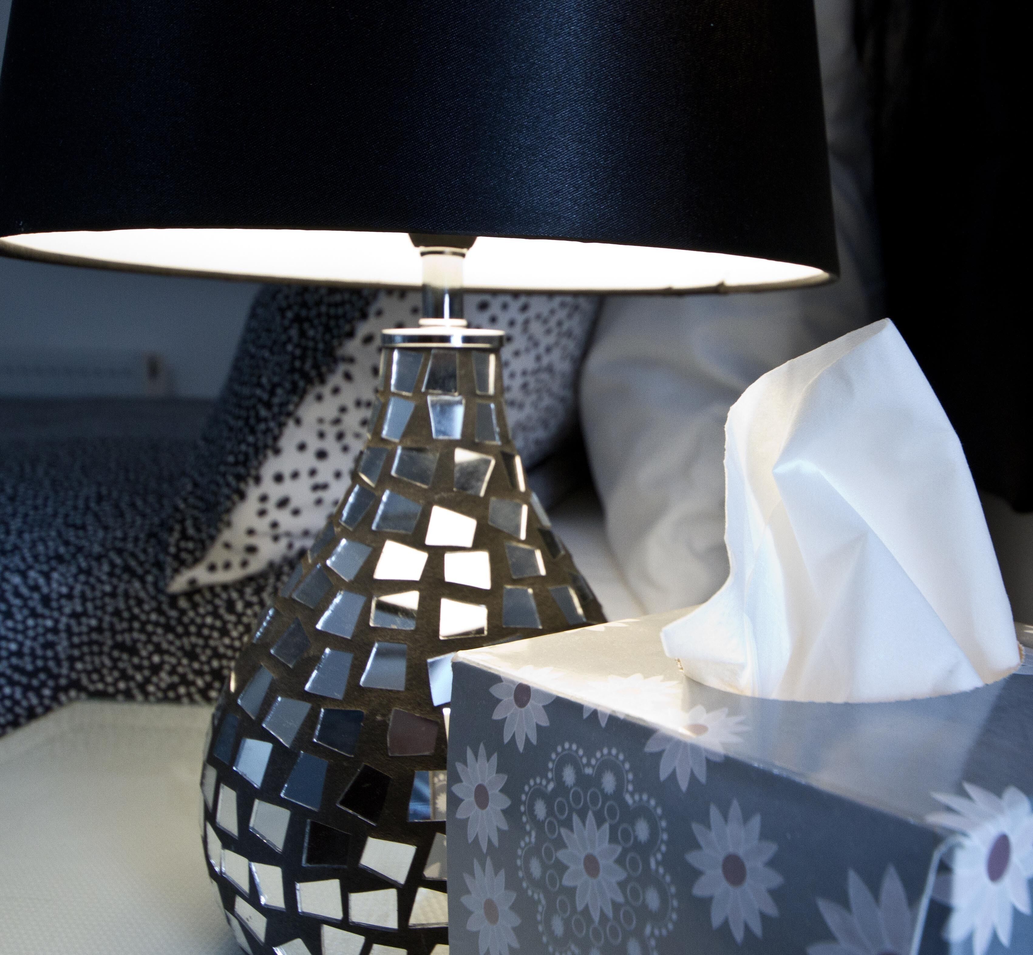 A bedside lamp with a mosaic design, a tissue box, and a patterned pillow.
