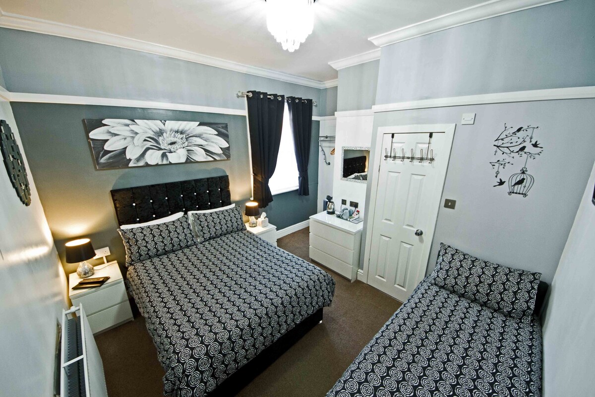 A bedroom with a large bed, a smaller bed, a nightstand, a dresser, a mirror, and a door with a bird and tree decal.