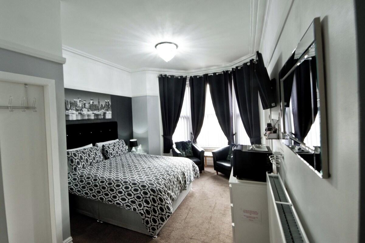 A modern bedroom with a large bed, a desk, a chair, and a mirror.