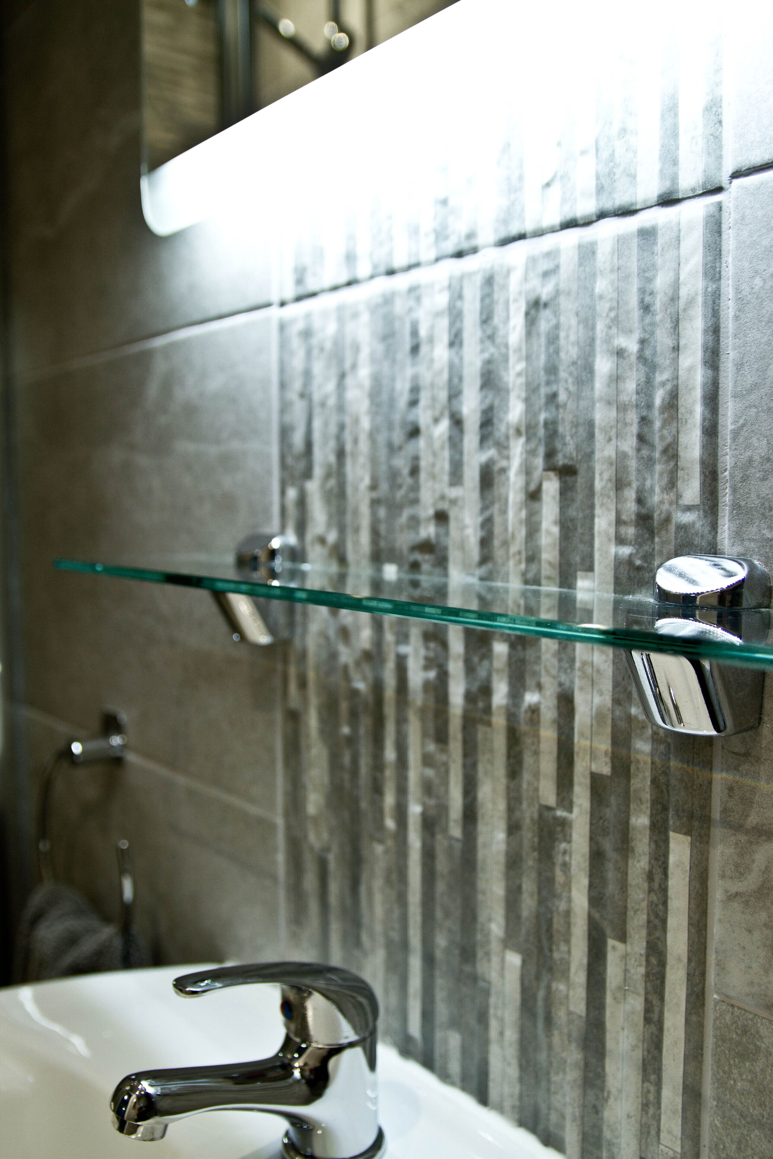 A bathroom with a glass shelf, a chrome faucet, and a textured wall.