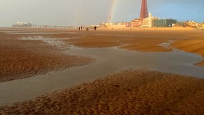 Uma praia com um farol e um arco-íris.