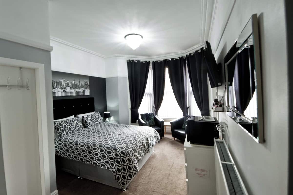 A modern bedroom with a large bed, a desk, a chair, and a mirror.