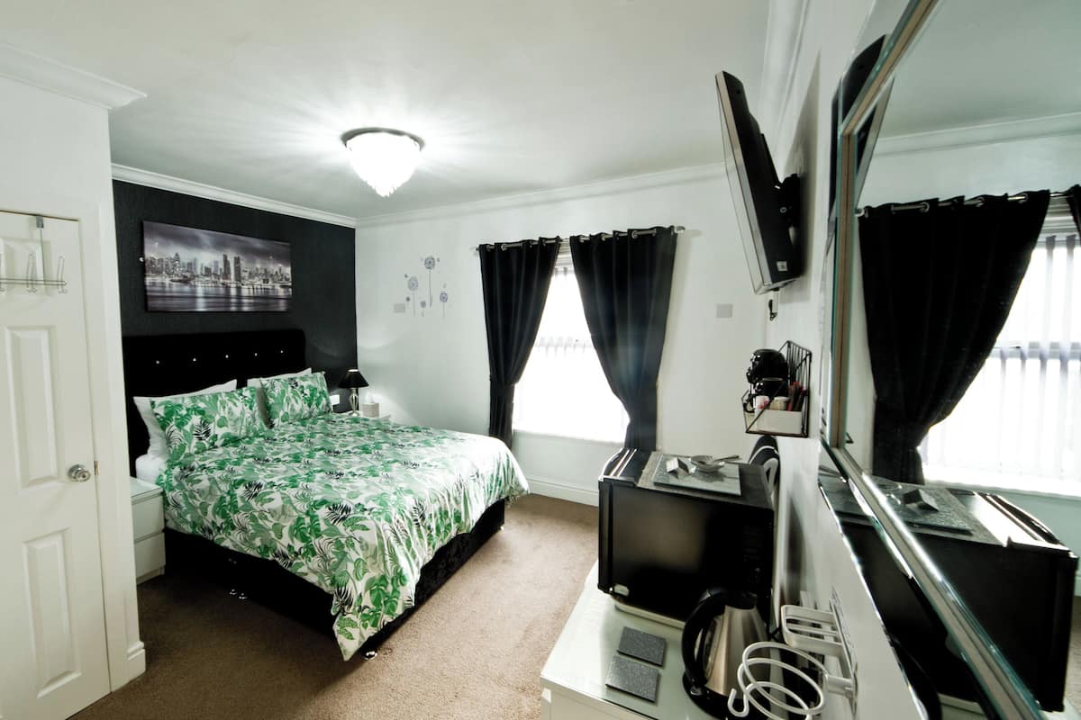 A bedroom with a bed, a TV, a mirror, and a window with curtains.