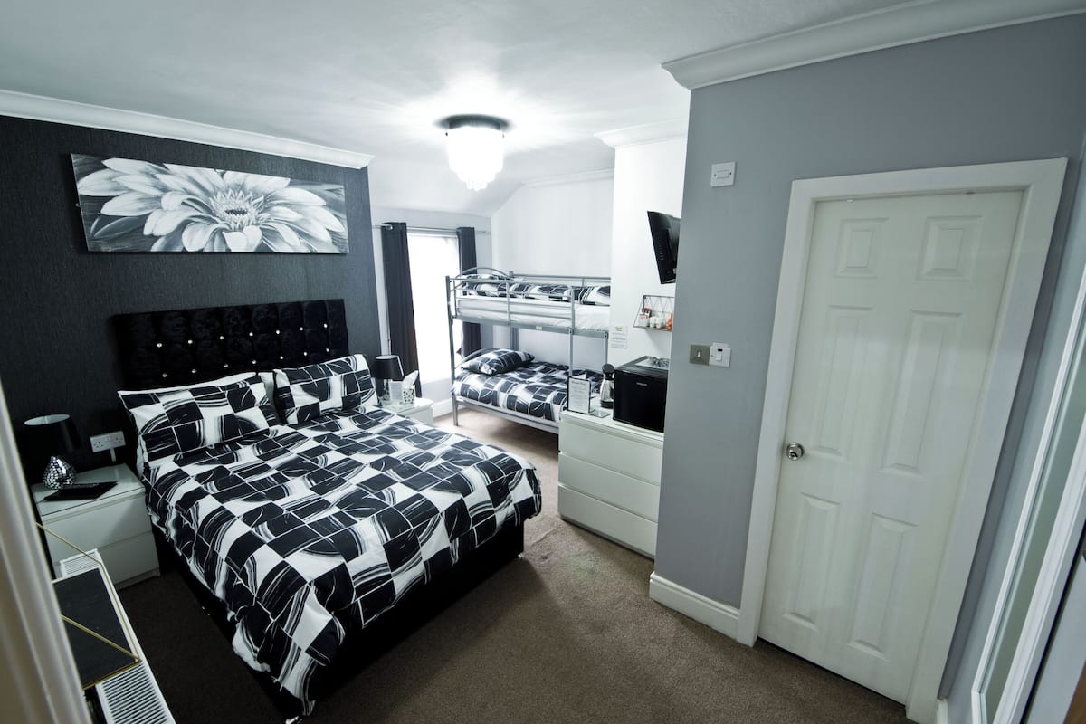 A bedroom with a large bed, a smaller bed on a bunk, a dresser, a TV, and a door.