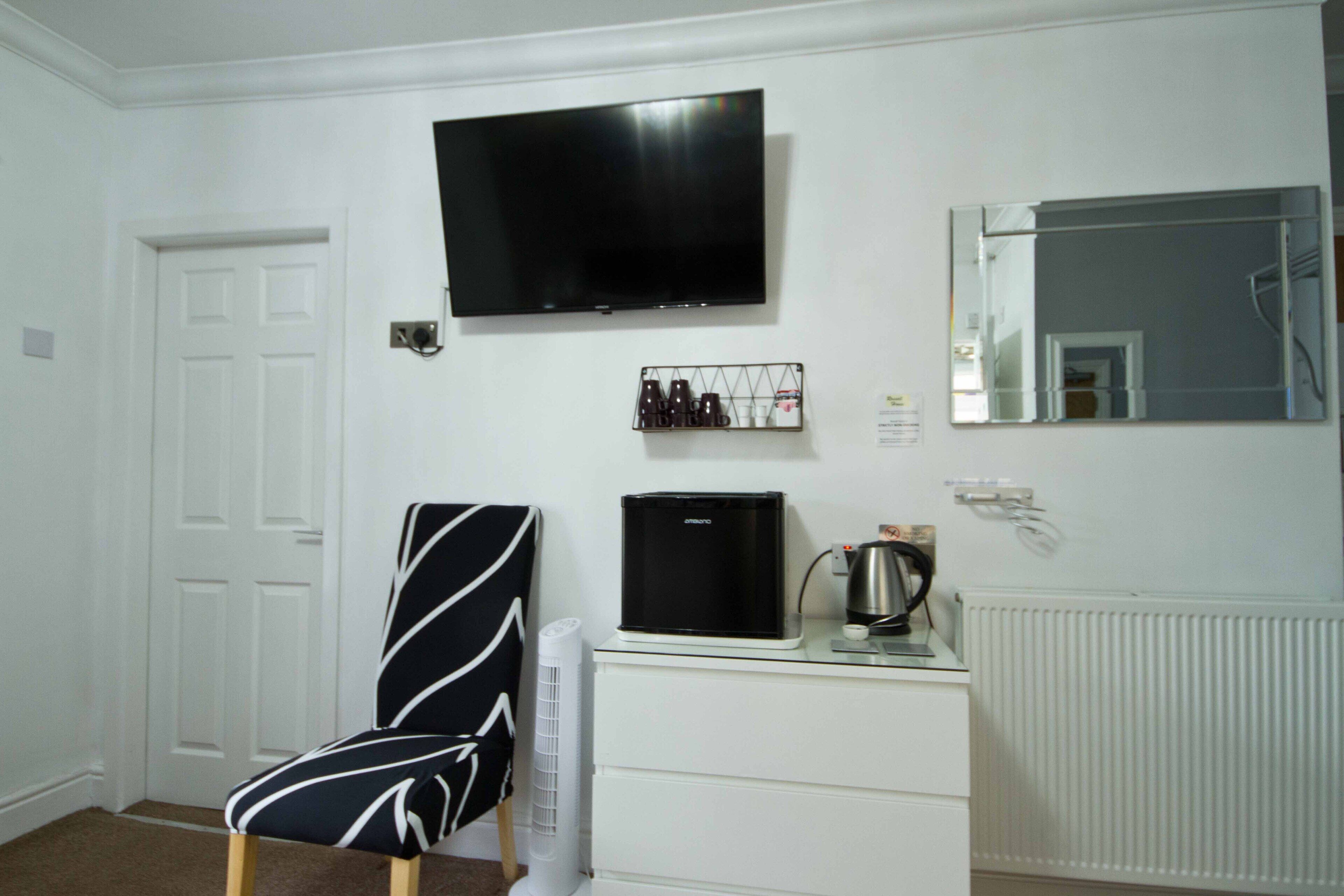 A room with a white door, a black and white striped chair, a flat-screen TV, a coffee maker, and a radiator.