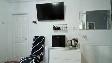 A room with a white door, a black and white striped chair, a flat-screen TV, a coffee maker, and a radiator.
