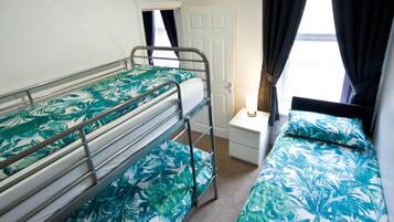 A room with bunk beds, a bedside table, a lamp, and a window with curtains.