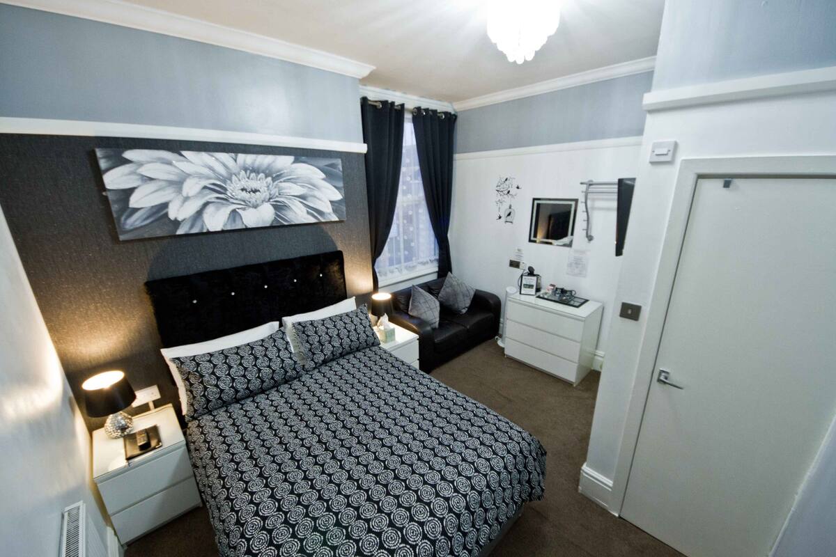 A bedroom with a bed, a nightstand, a dresser, a TV, and a door.