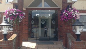 A building entrance with a 'Welcome' sign, glass doors, and flower baskets on either side. - Royal Hotel (Norwich)