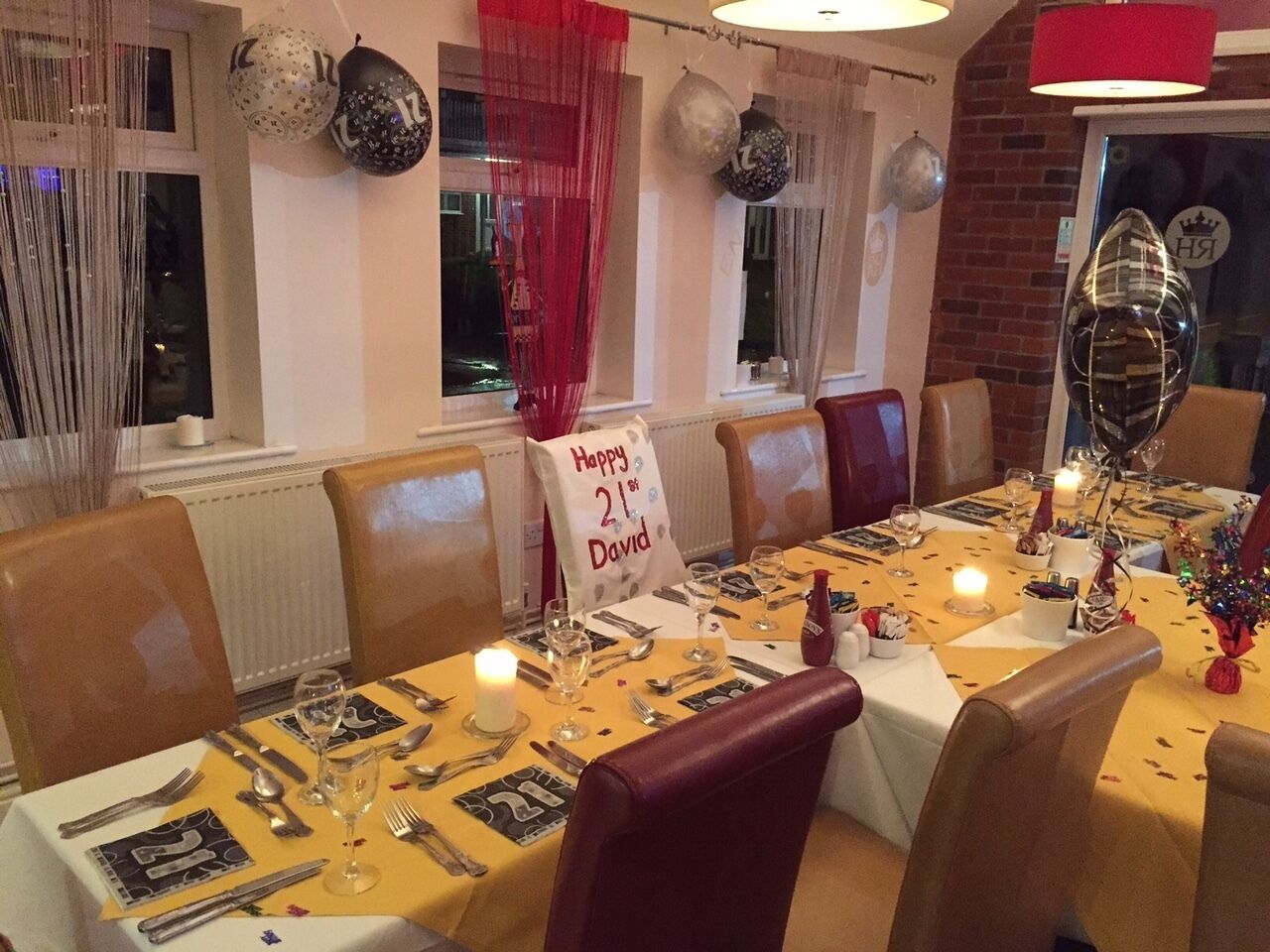A dining table set for a meal with a 'Happy 21st David' sign, candles, and a festive atmosphere with balloons and decorations.