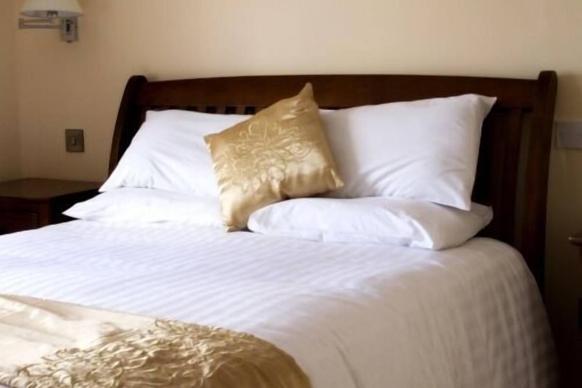 Una cama bien hecha con sábanas blancas y una única almohada decorativa.