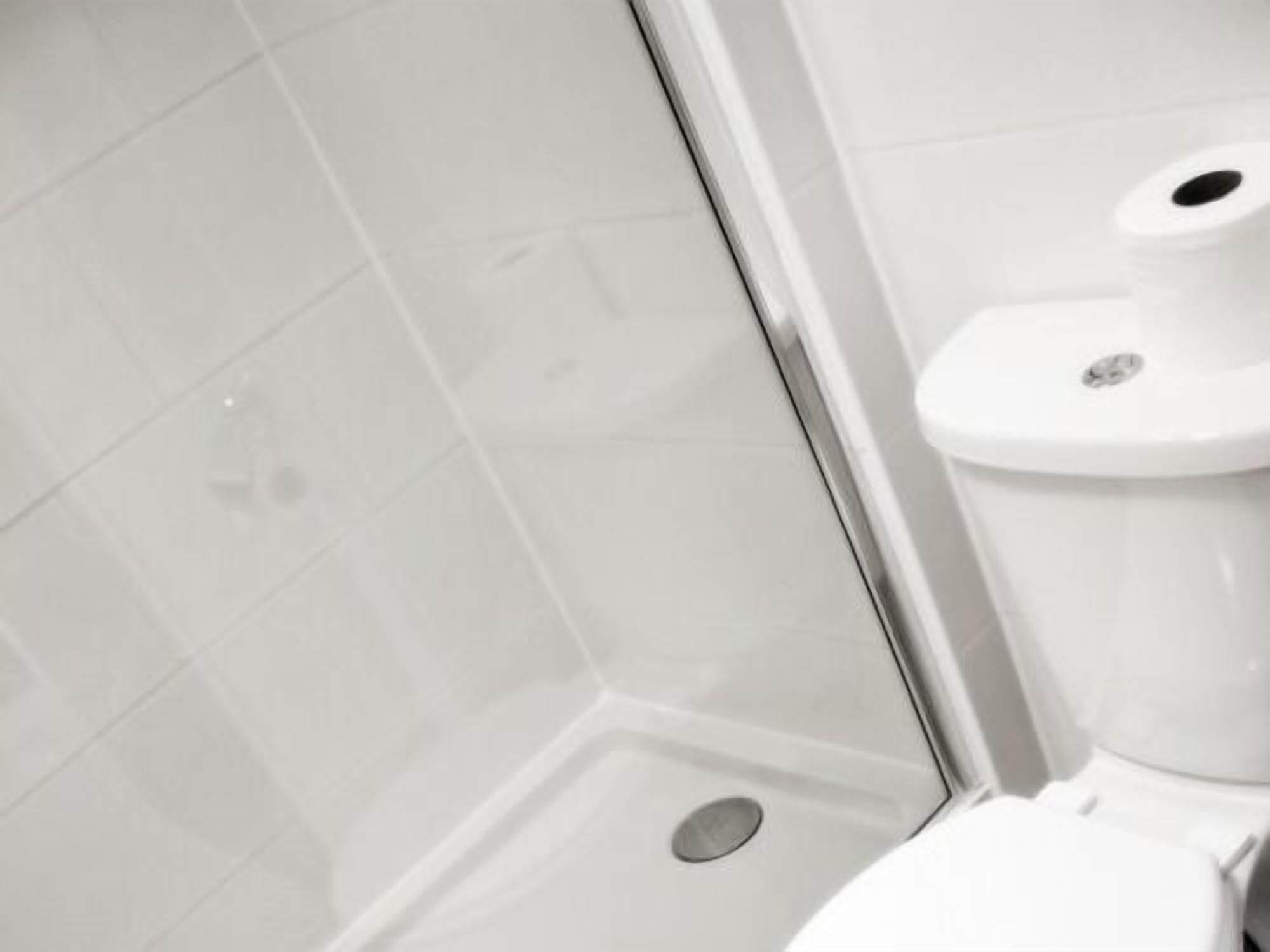 Eine weiße Toilette mit Bidet-Befestigung in einem Badezimmer mit weißen Fliesen.