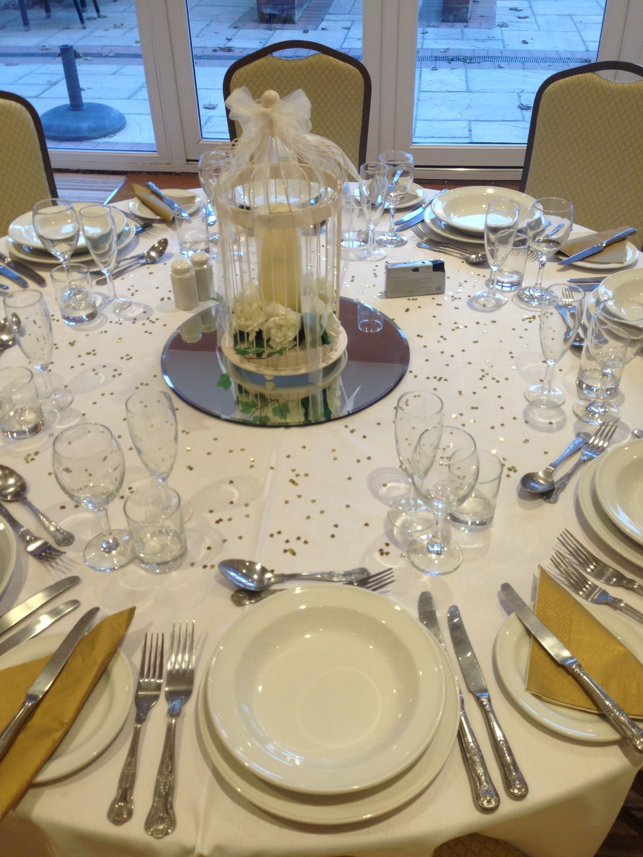 Una mesa dispuesta para un evento formal, con cristalería transparente, cubiertos y un centro de mesa decorativo.