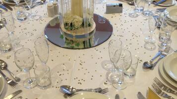 Una mesa dispuesta para un evento formal, con cristalería transparente, cubiertos y un centro de mesa decorativo.