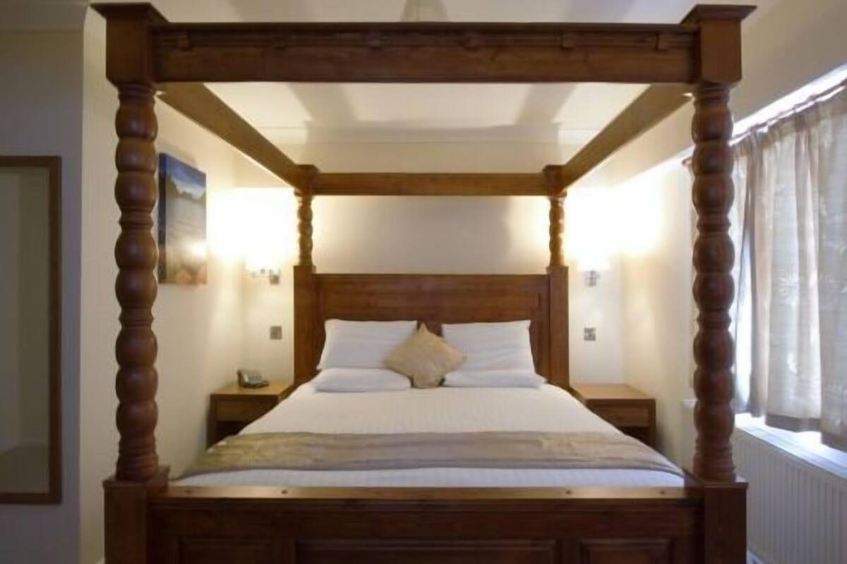 Una cama con dosel de madera, ropa de cama blanca y una mesita de noche con una lámpara.