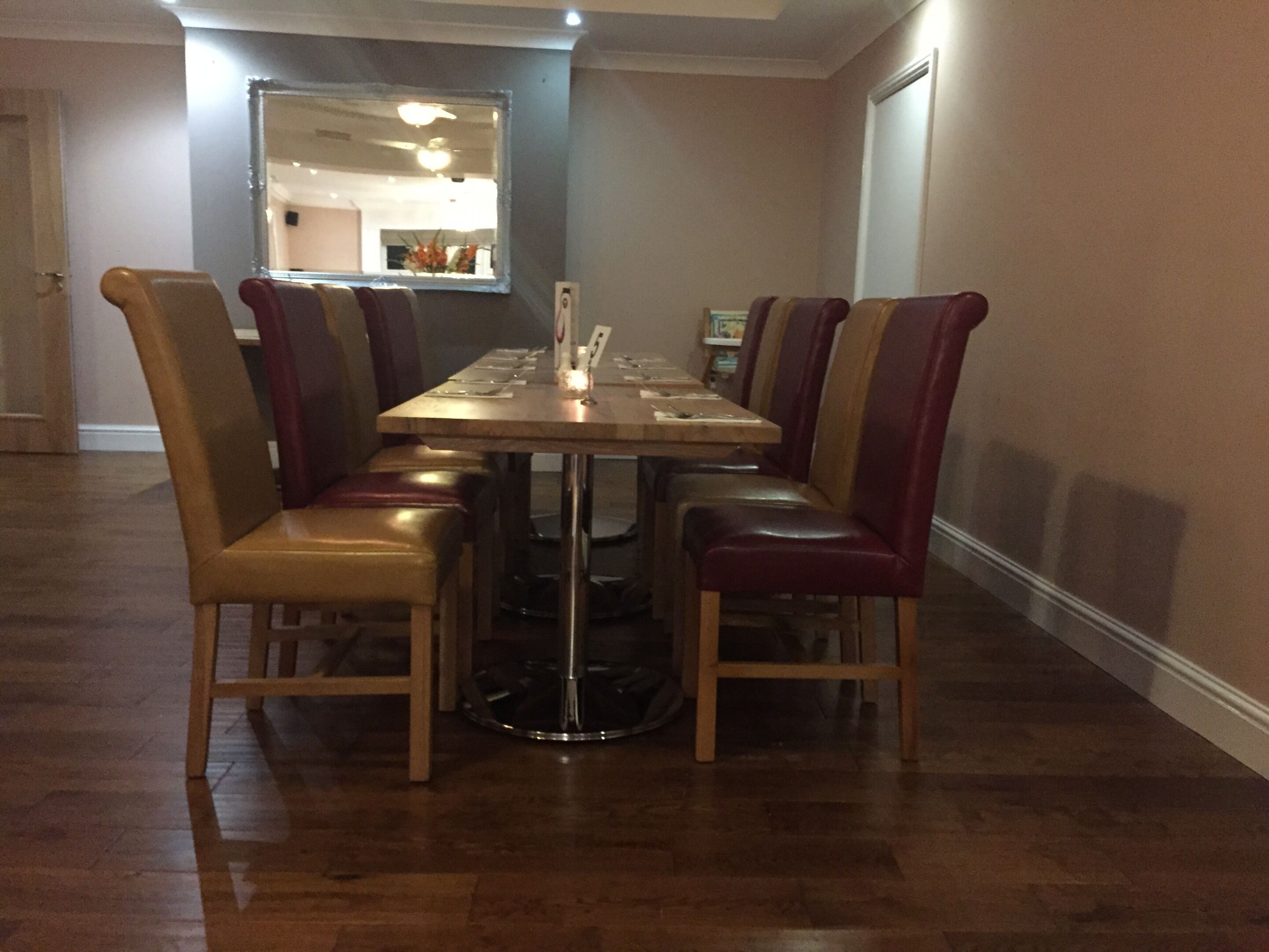 A dining area with a rectangular table surrounded by six chairs with cushioned seats. The floor is wooden, and there is a mirror on the wall above the table.
