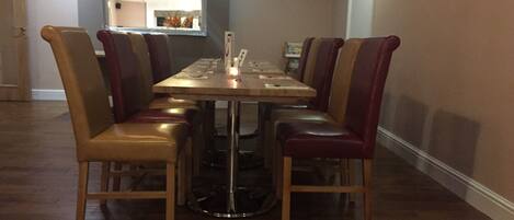 A dining area with a rectangular table surrounded by six chairs with cushioned seats. The floor is wooden, and there is a mirror on the wall above the table.
