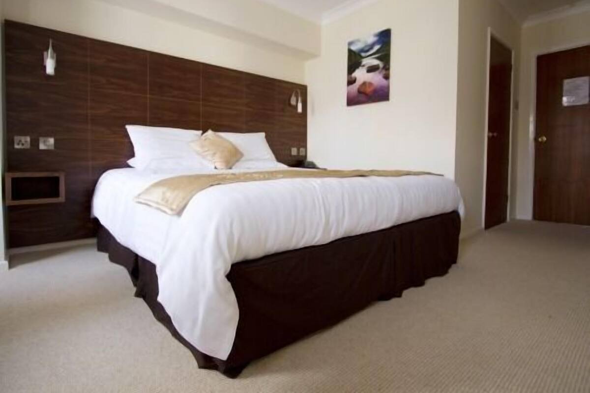 Una cama bien hecha con ropa de cama blanca y un cabecero oscuro en una habitación de hotel.