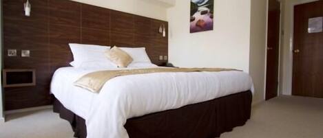 A neatly made bed with white bedding and a dark headboard in a hotel room.