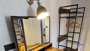 A compact room with a wooden vanity, a mirror, a desk, and a metal shelving unit. - The Crown Inn (Marlborough)