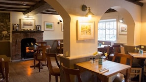 A cozy dining area with wooden tables and chairs, a fireplace, and framed artwork on the walls. - The Crown Inn (Marlborough)