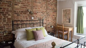 A bedroom with a brick wall, a metal bed frame, a wooden desk, and a chair. - The Crown Inn (Marlborough)