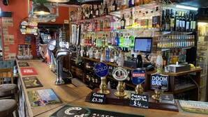 A bar with multiple taps, shelves of liquor bottles, and a menu board. - The Crown Inn (Marlborough)