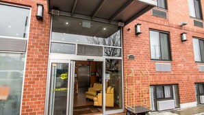 L’entrée d’un hôtel, avec une porte en verre, un paillasson et une chaise jaune à l’extérieur.