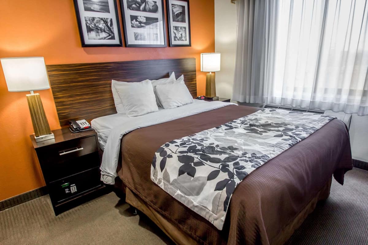 Une chambre d’hôtel avec un grand lit, deux tables de chevet avec des lampes, une petite table de nuit avec un téléphone et des tableaux encadrés au mur.
