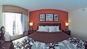 Une chambre d’hôtel avec un grand lit, deux tables de chevet avec des lampes, une fenêtre avec des rideaux et trois tableaux encadrés accrochés au mur.