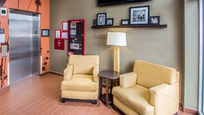 Un hall d’hôtel avec deux fauteuils, une petite table, un téléviseur fixé au mur, un détecteur d’incendie et un réfrigérateur.