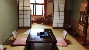 Una habitación japonesa tradicional con suelo de tatami, una mesa baja con cojines y puertas correderas shoji.