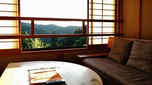 Una habitación con sofá y mesa, una ventana con vistas a un área boscosa y una tradicional pantalla japonesa shoji.