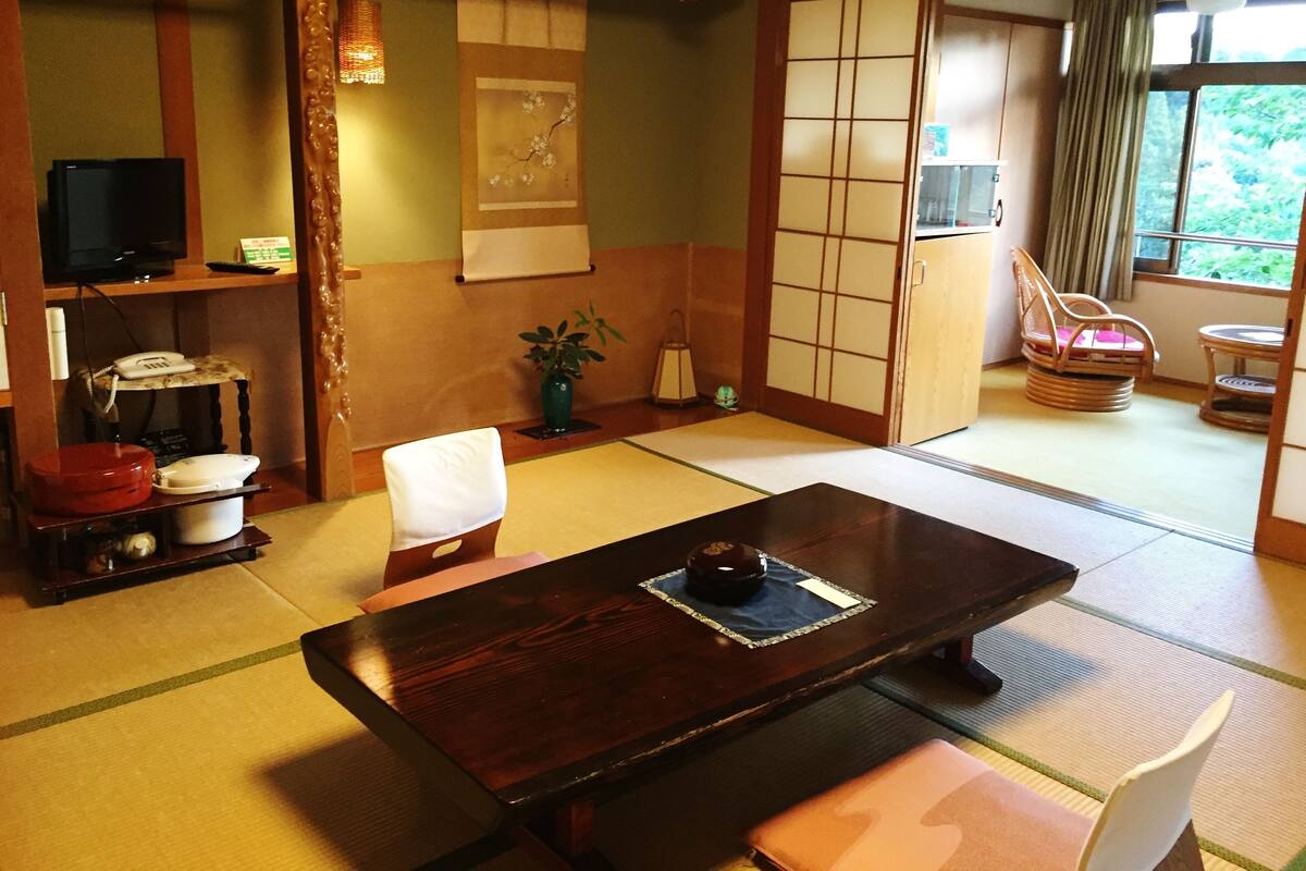 Perinteinen japanilainen huone, jossa on tatamimatto, matala pöytä, tuoli, televisio, puhelimen sisältävä hylly ja liukuovi, joka johtaa toiseen huoneeseen.