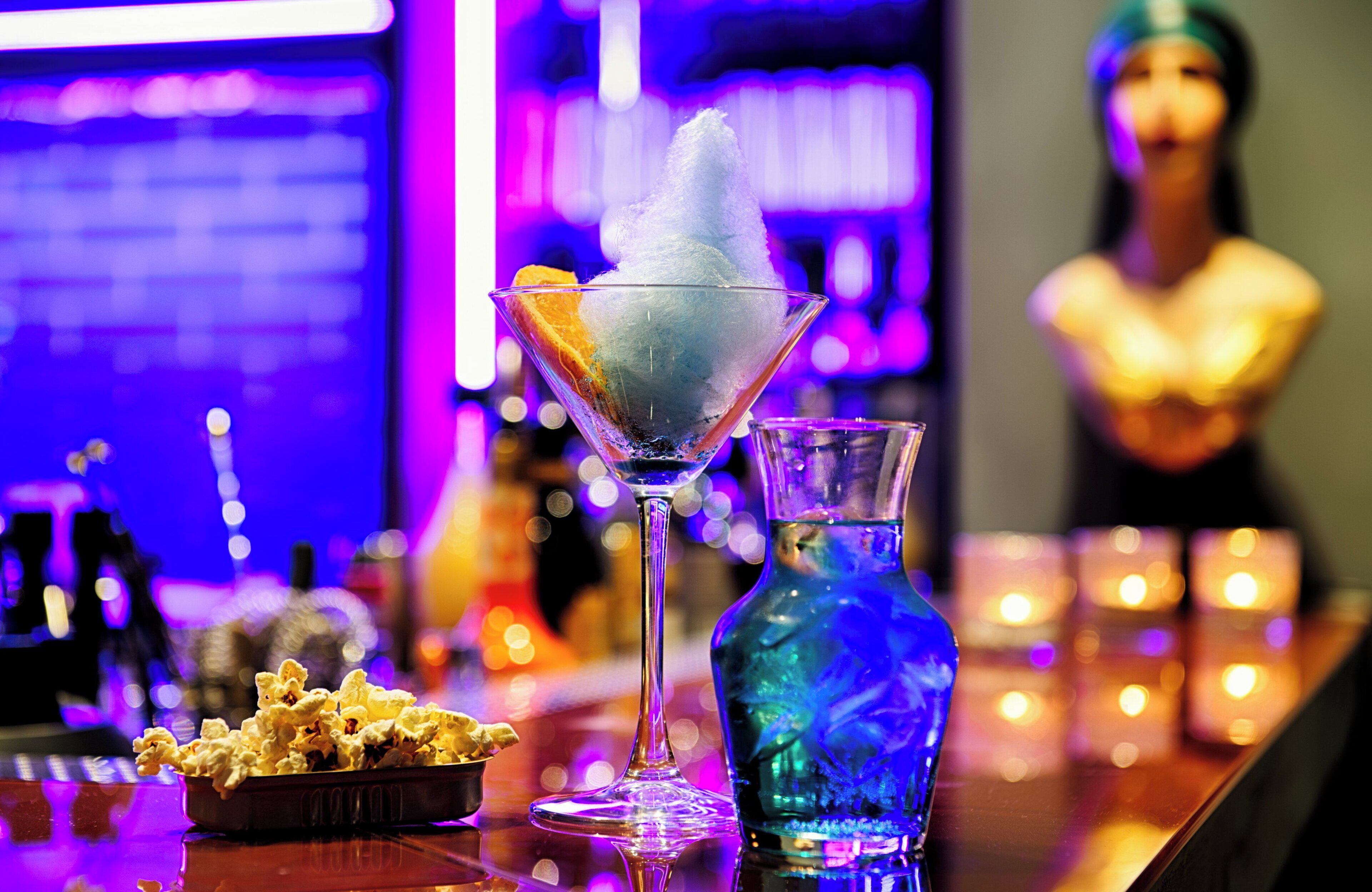 A bar setting with a martini glass, a blue bottle, and a bowl of popcorn.