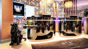 A NYX Hotels reception area with a modern design, featuring a large digital sign, a piano, and a reflective reception desk. - NYX Hotel Mannheim by Leonardo Hotels (Mannheim)