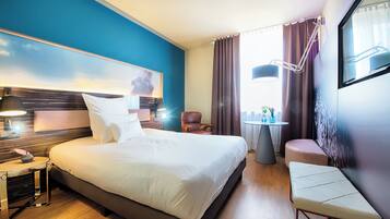 Habitación de hotel con una cama grande, lámparas de noche, una mesita con lámpara, una silla y un banco.
