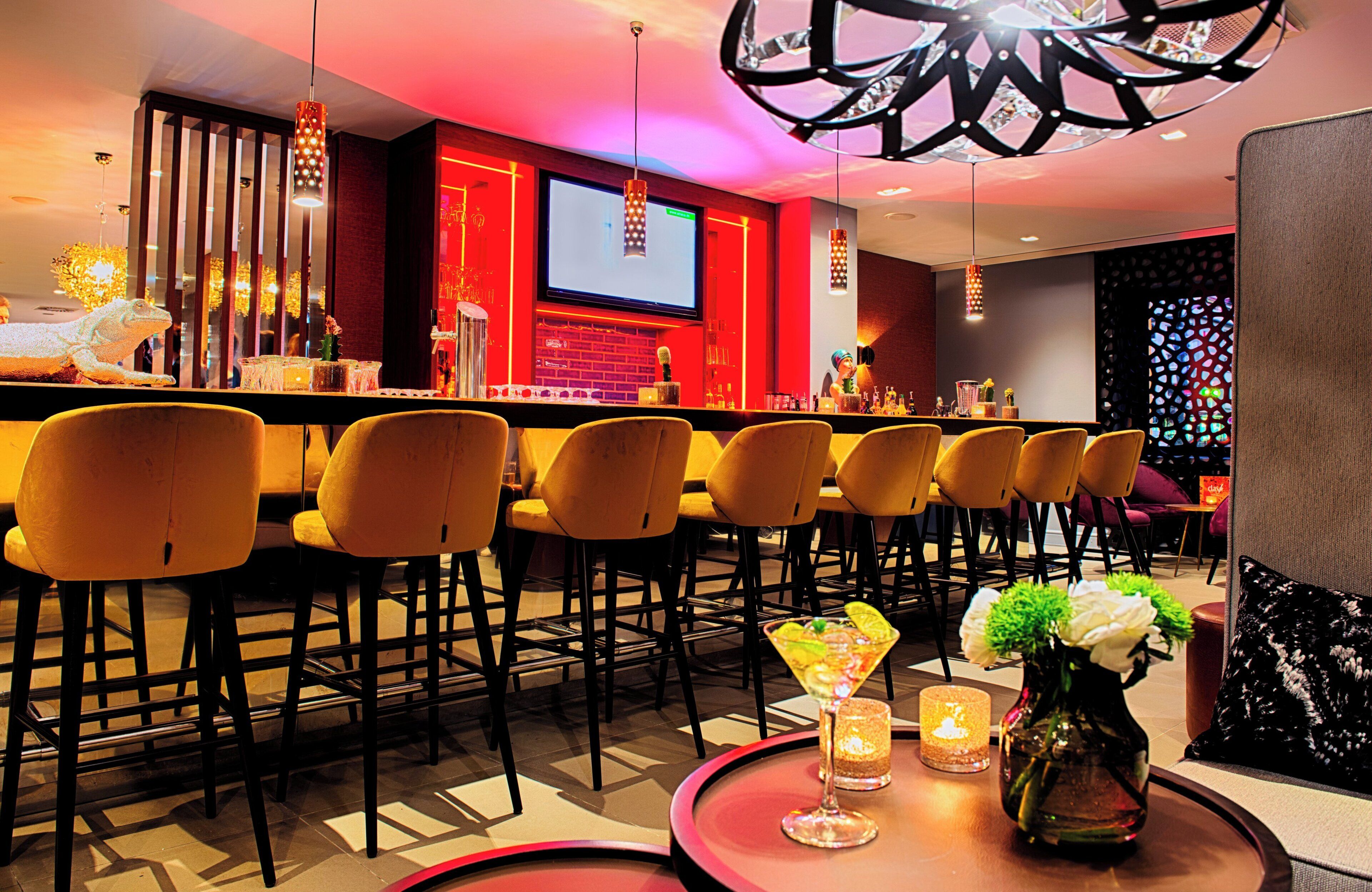 Zona de bar con sillas amarillas, una pantalla de televisión y una lámpara decorativa.