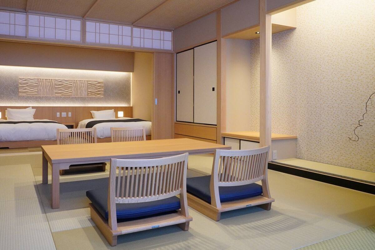 A hotel room with two beds, a dining table, and chairs.