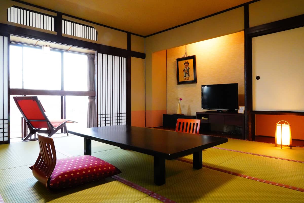 A traditional Japanese room with tatami flooring, a low table, a television, and sliding doors.