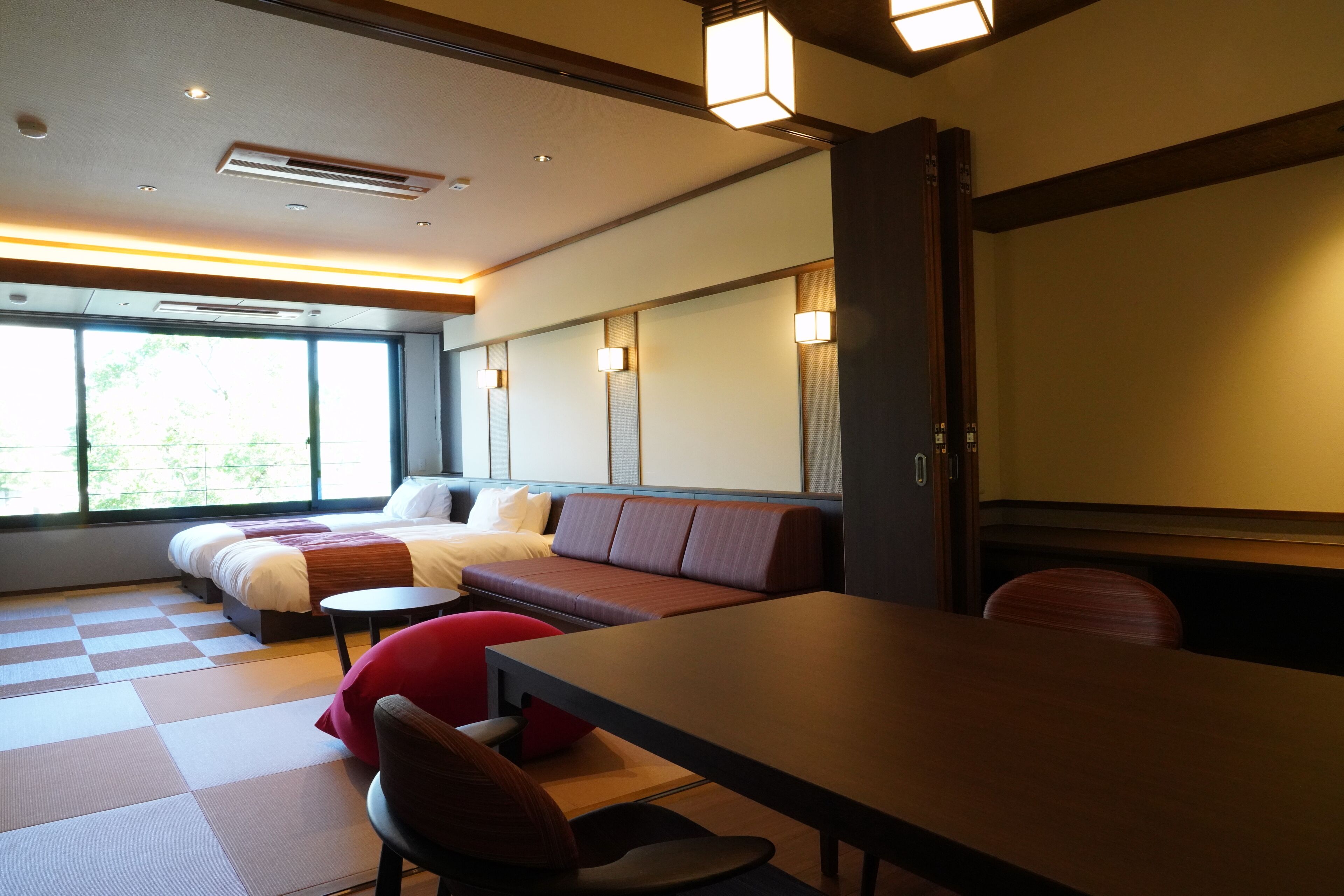 Habitación de hotel moderna con una cama grande, un sofá, una mesa de comedor y vistas a zonas verdes.