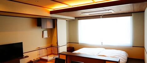 A hotel room with a bed, a TV, a desk, and a window.