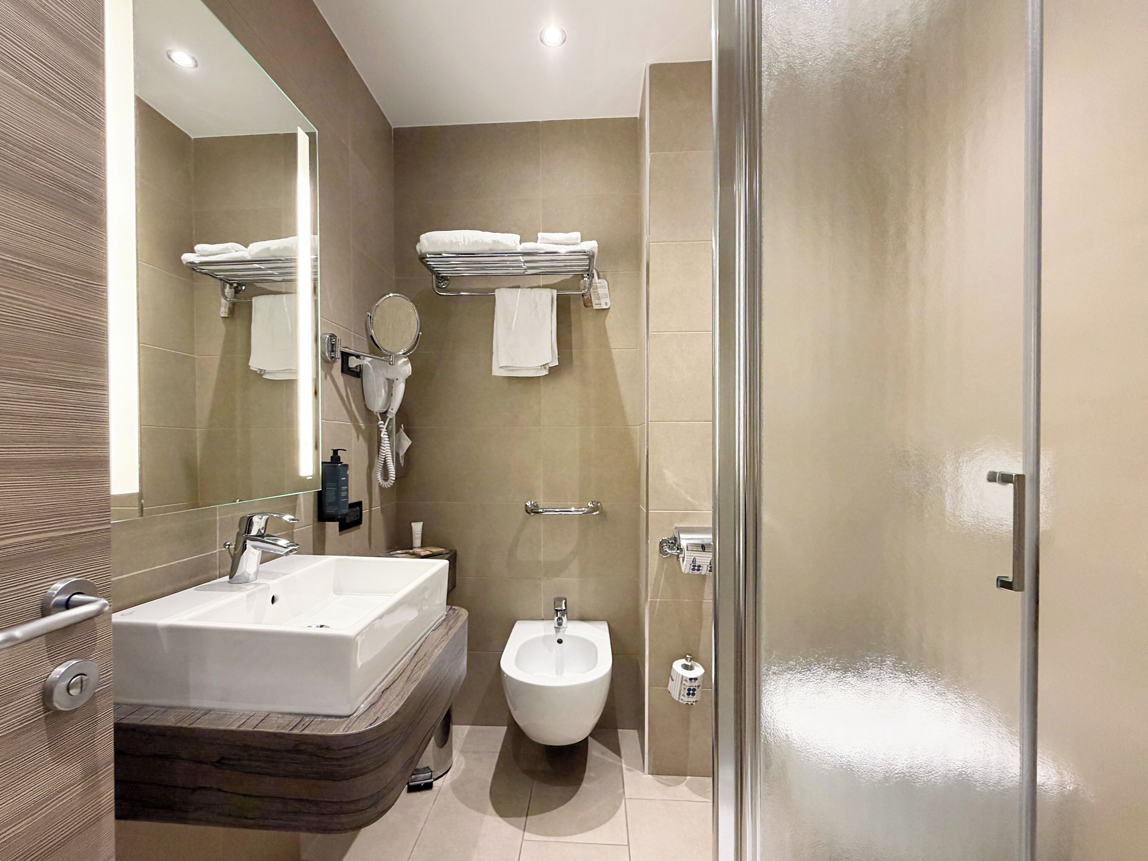 A modern bathroom with a large sink, bidet, and a glass shower enclosure.