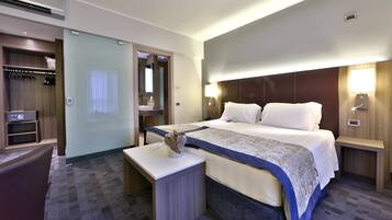 A hotel room with a large bed, bedside tables, a desk, a wardrobe, and a mirror.