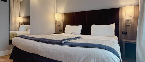 Una habitación de hotel moderna con una cama grande, suelo de madera y cabecera integrada.