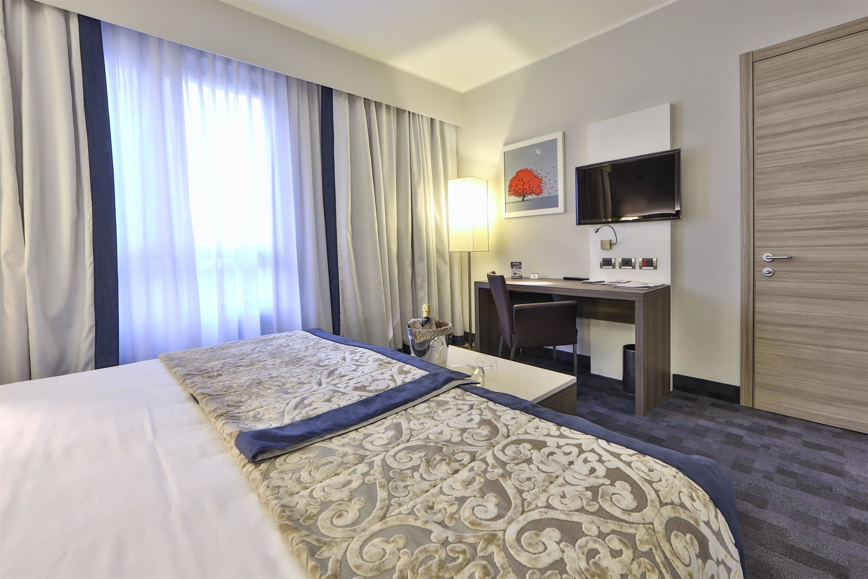 Une chambre d’hôtel avec un lit, un bureau, une chaise, une télévision et une porte.